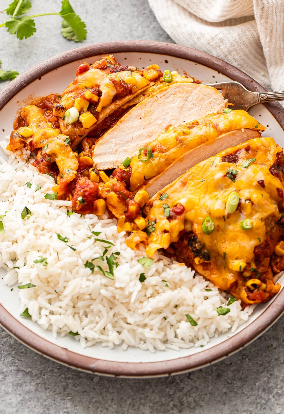 Sliced chicken breast topped with salsa and melted cheese on a white plate with rice.