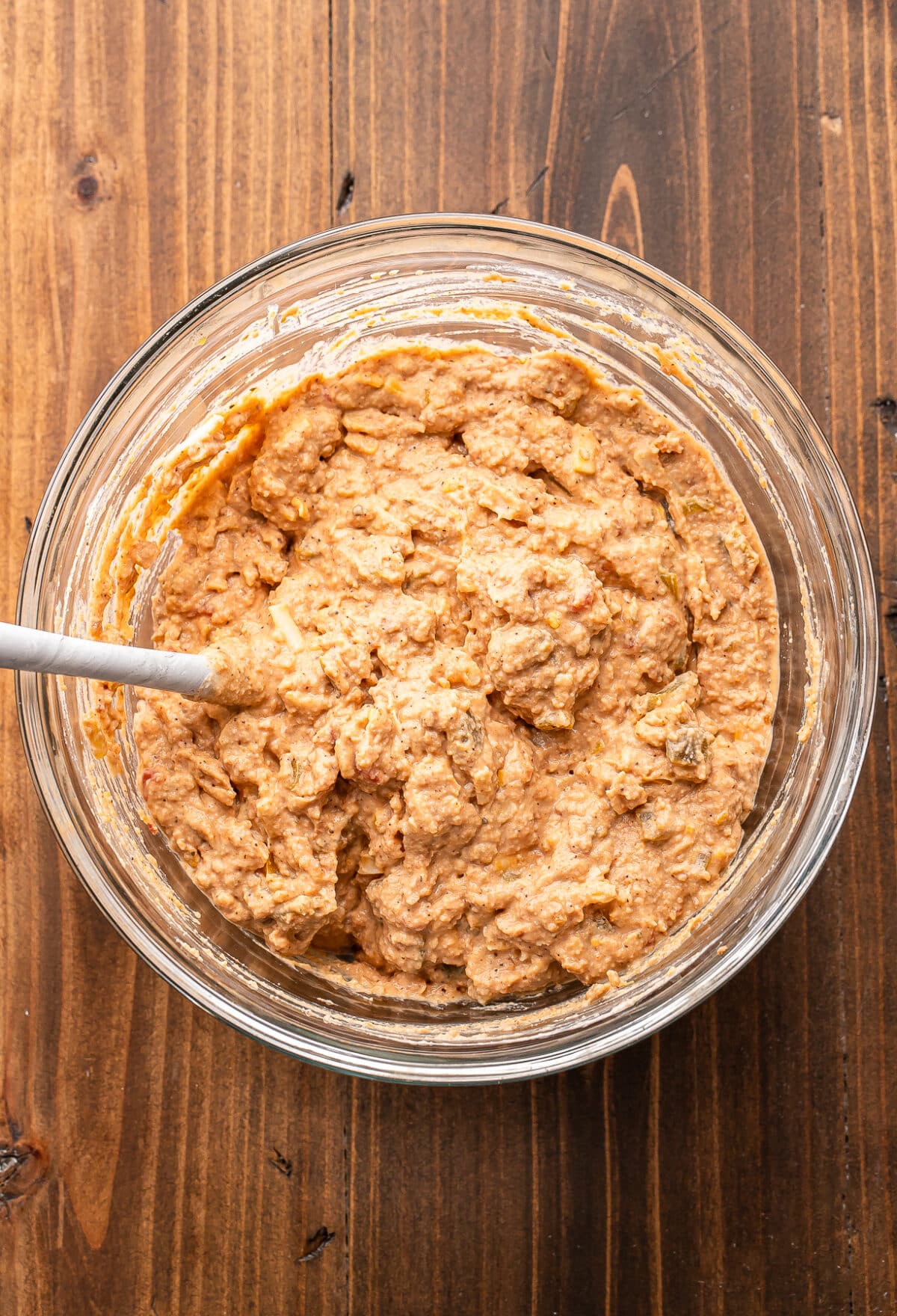 Bean dip mixture in a glass bowl with a rubber spatula.