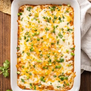 Cheesy bean dip in a white rectangular baking dish with a bowl of tortilla chips behind it.