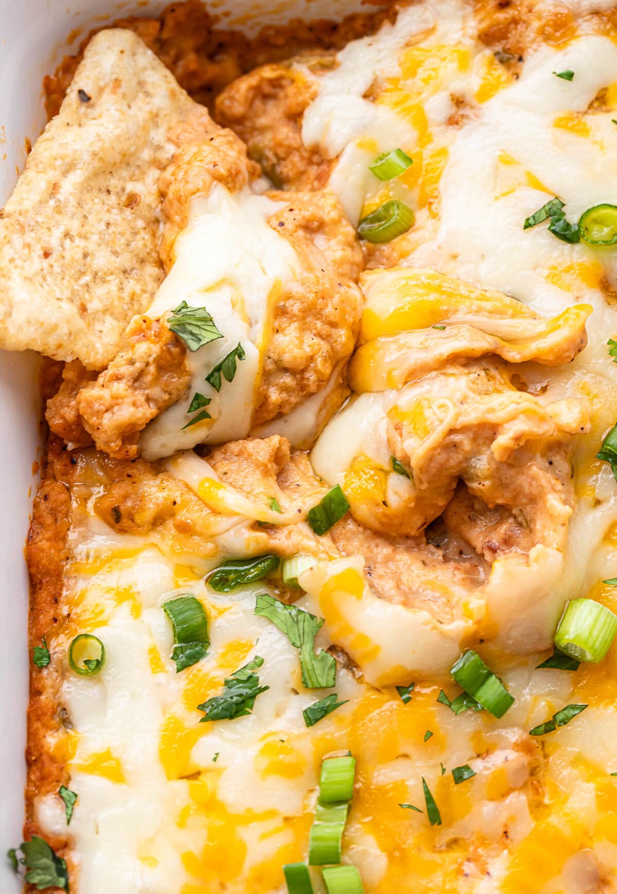 Tortilla chip scooping up cheesy bean dip.