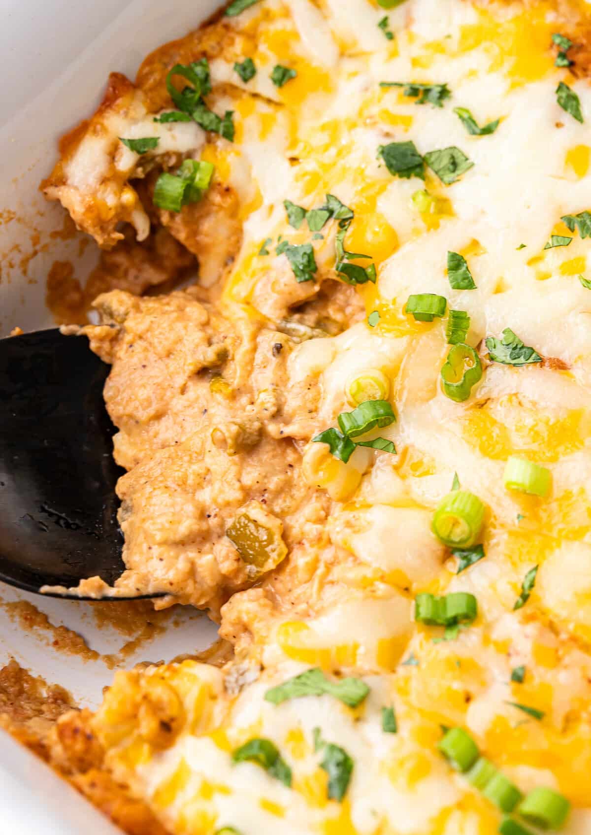 Cheesy bean dip in a white baking dish with a black serving spoon.