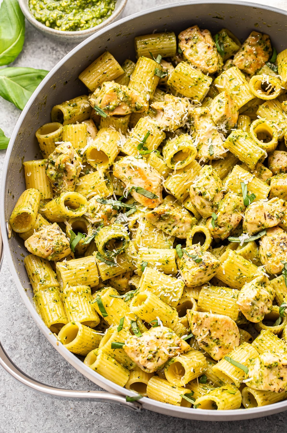 Chicken pesto pasta with parmesan cheese in a saute pan.