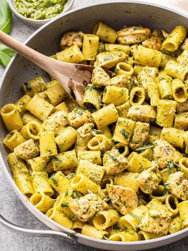 Chicken pesto pasta in a saute pan with a wooden serving spoon.