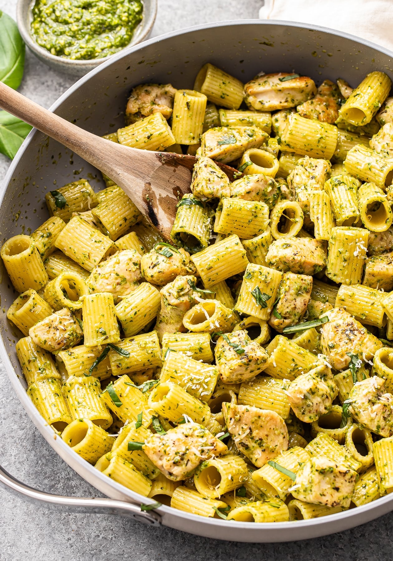 Chicken pesto pasta in a saute pan with a wooden serving spoon. 