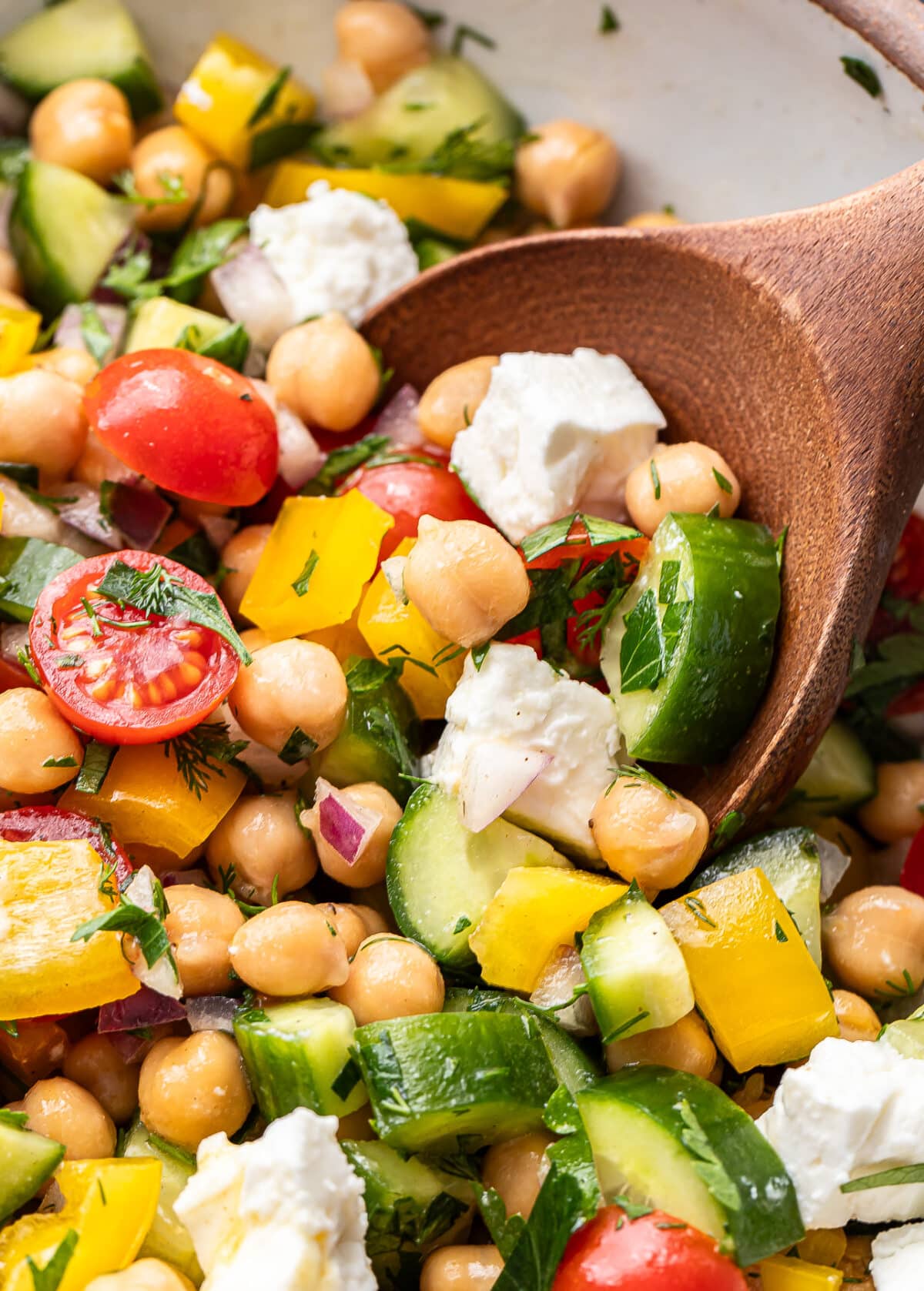 Wooden spoon scooping up the chickpea salad out of a white salad bowl.