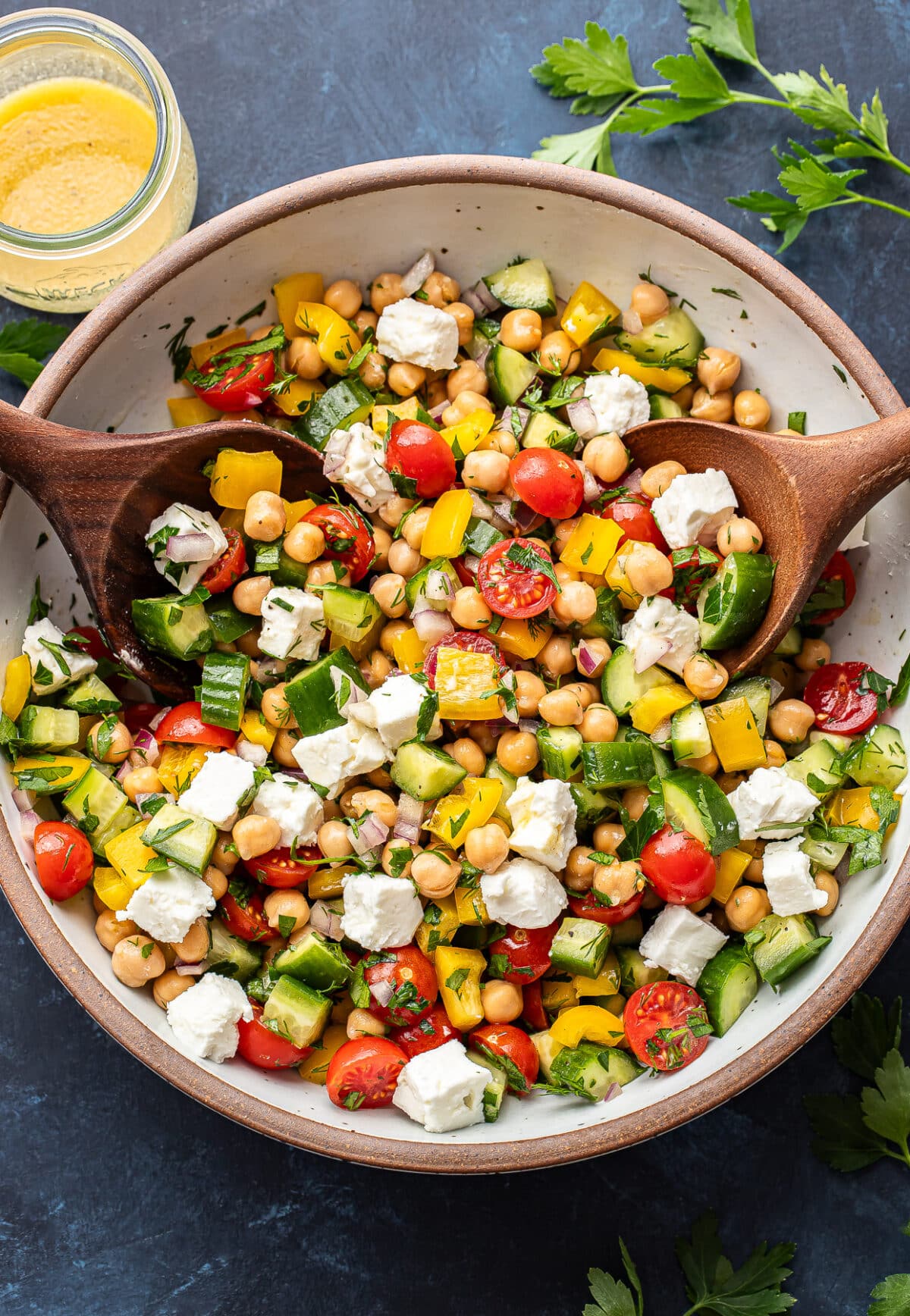 Chickpea salad in a white salad bowl with two wooden serving spoons.