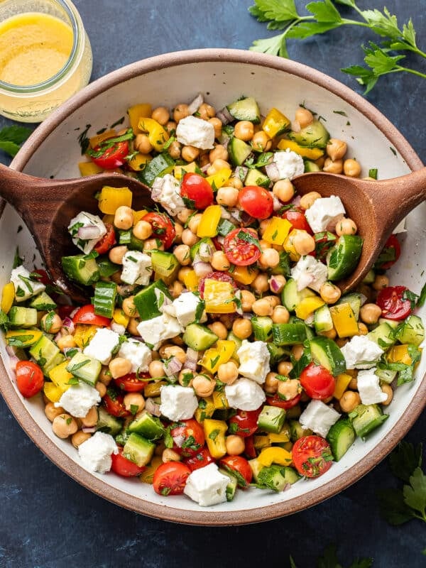Chickpea salad in a white salad bowl with two wooden serving spoons.