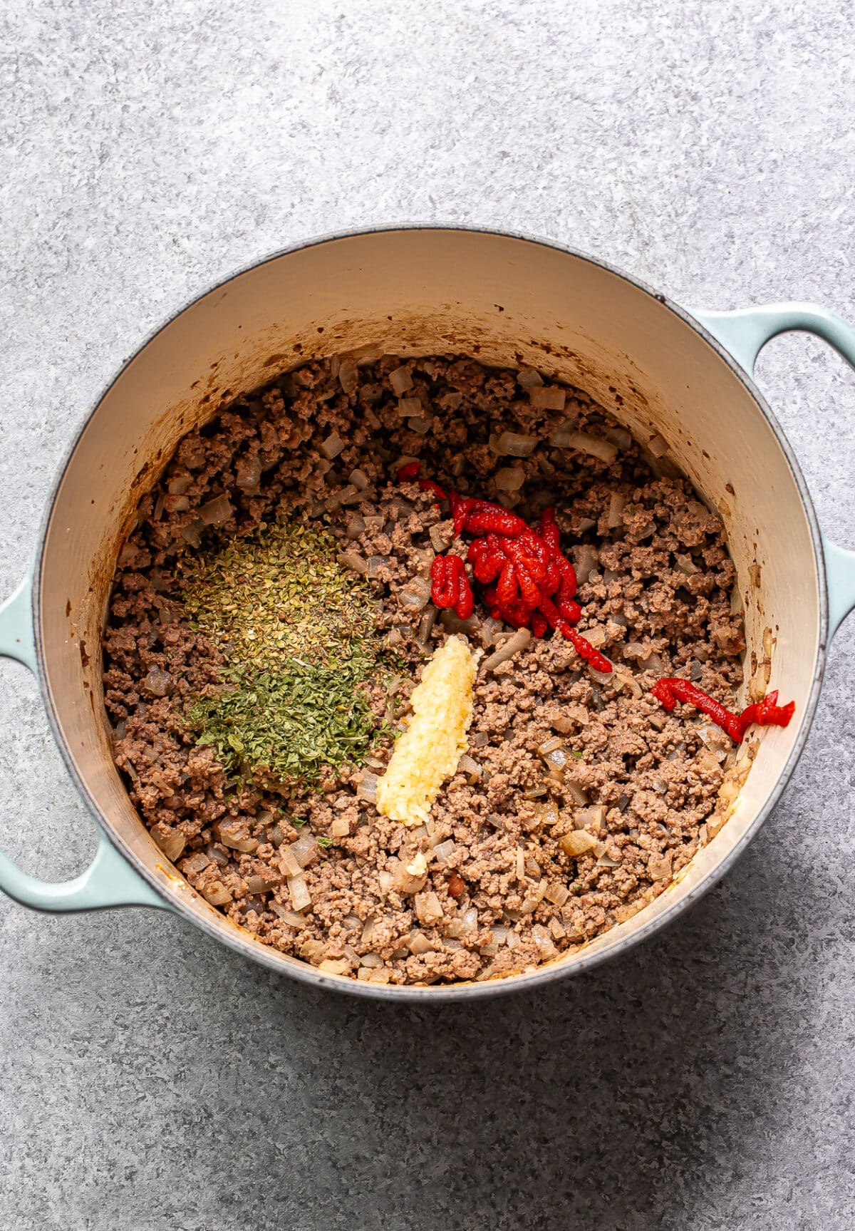 Ground beef, onions, garlic, dried herbs, and tomato paste in a pot.