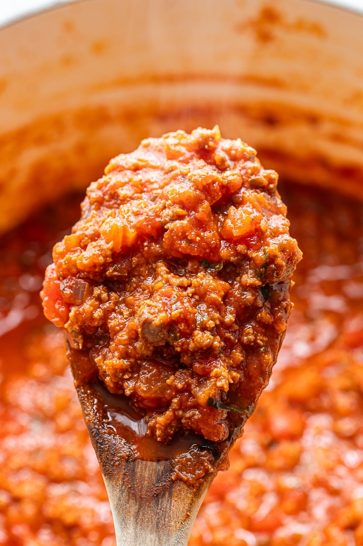 Wooden spoon holding up a scoop of homemade spaghetti sauce.