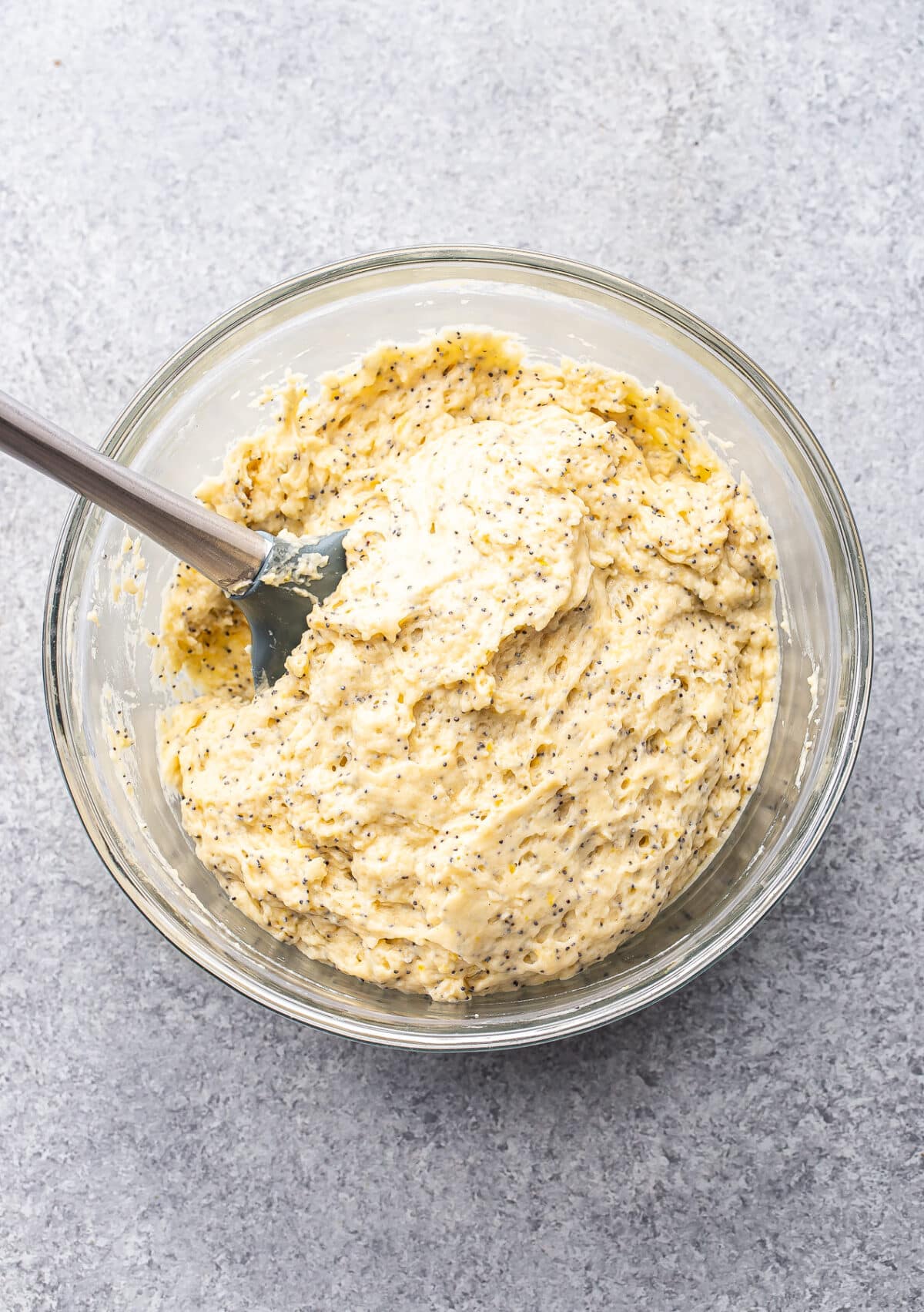 Lemon poppy seed muffin batter in a glass mixing bowl with a rubber spatula.