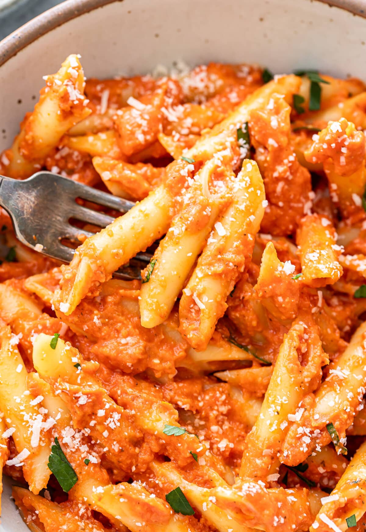 A fork picking up pasta alla vodka out of a white bowl.