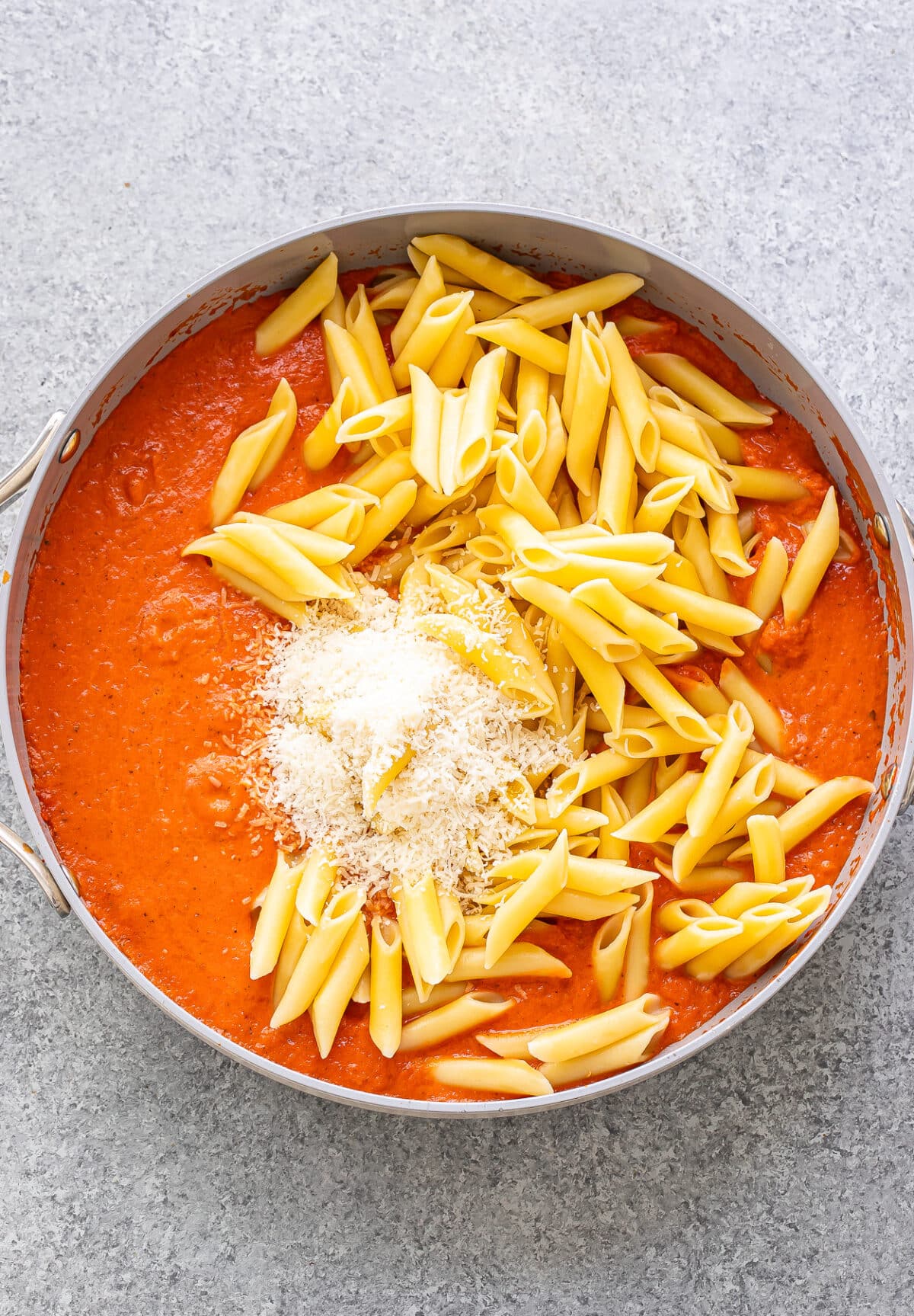 Vodka sauce, penne, and parmesan cheese in a skillet before it's been stirred together.