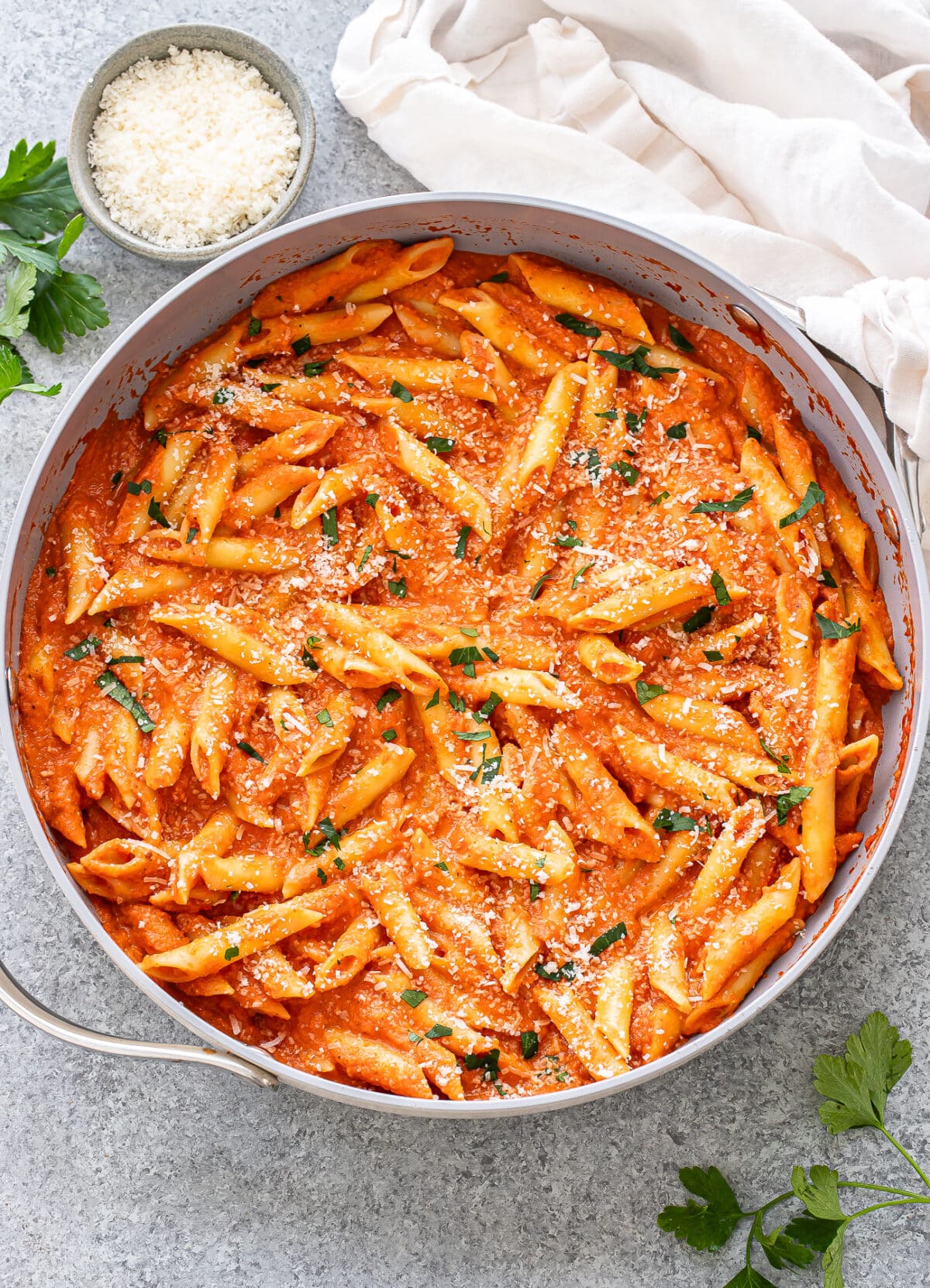 Penne alla vodka in a skillet topped with parmesan cheese and parsley.