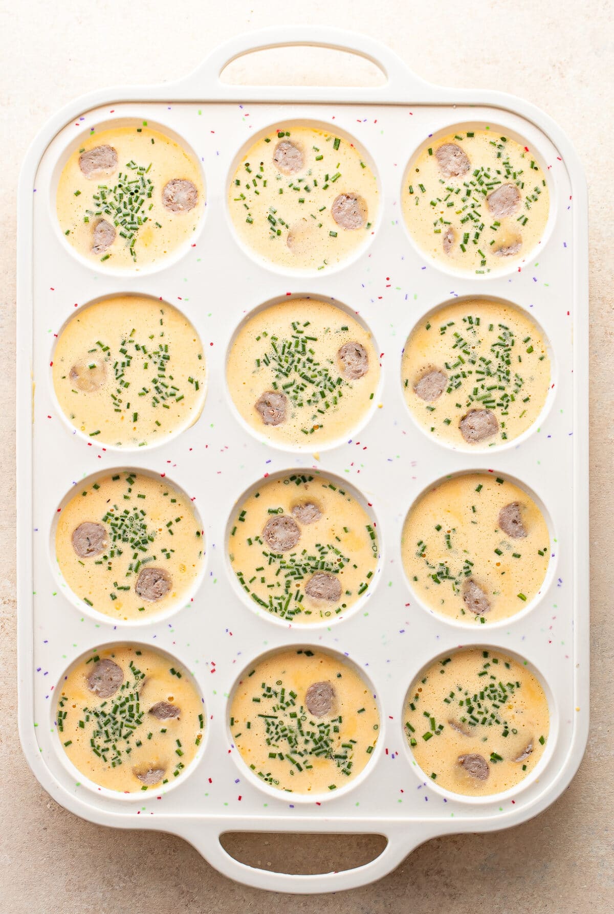 Uncooked cottage cheese egg bites with sausage and chives in a silicone muffin pan.
