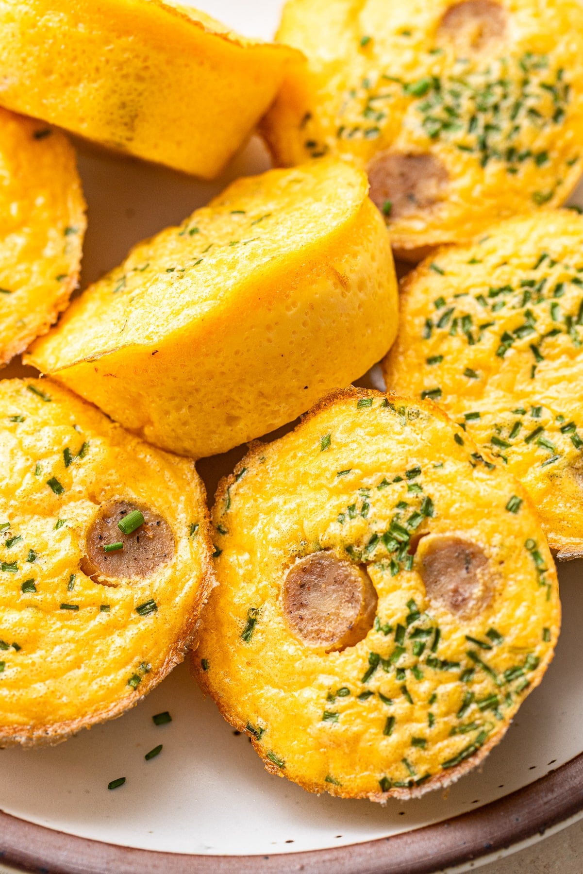 Egg bites with sausage and chives on a white plate.