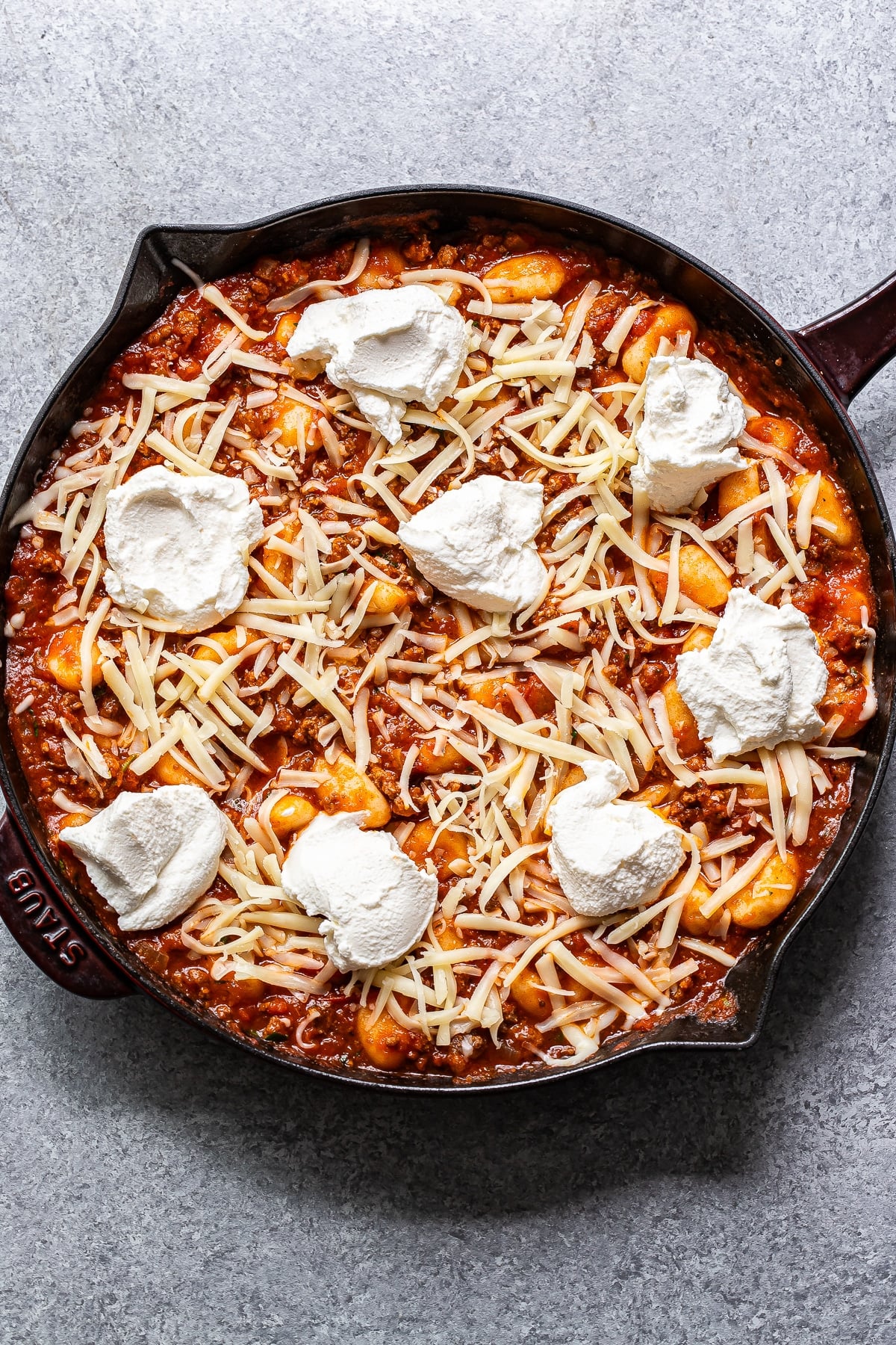 Ground beef, marinara sauce and gnocchi in a skillet topped with shredded mozzarella and ricotta before it's been baked.