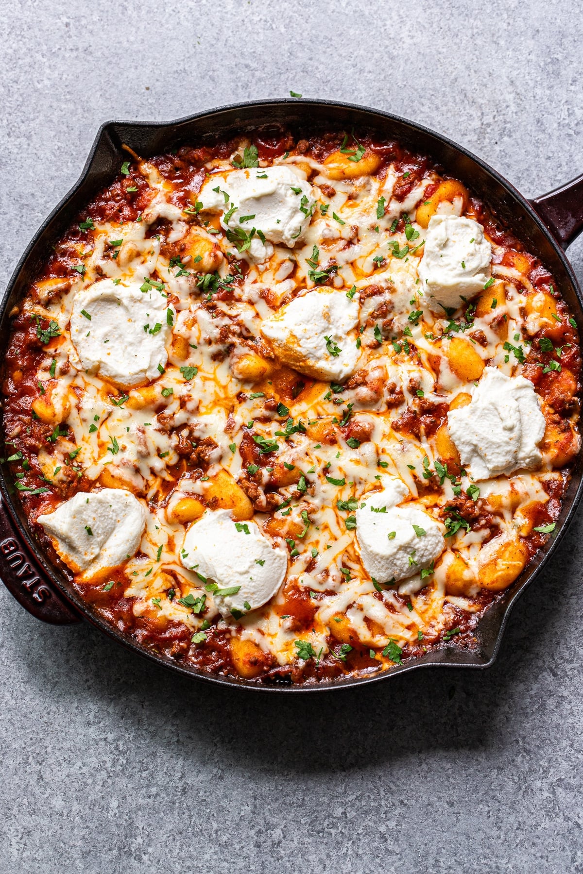 Baked gnocchi with ground beef and marinara sauce and topped with cheese and ricotta in a skillet.