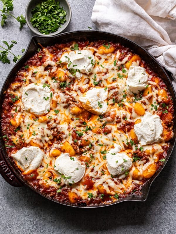 Baked Italian ground beef and gnocchi in a skillet. A bowl of chopped parsley is behind the skillet.