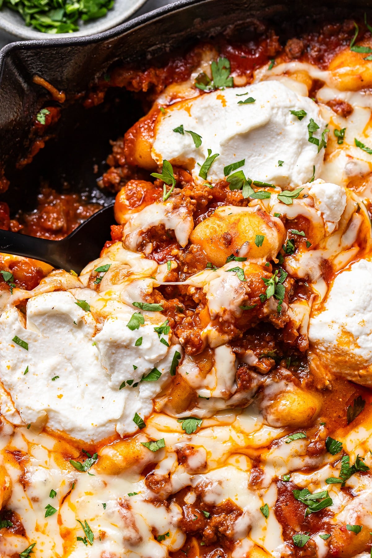 Cheesy baked ground beef and gnocchi with a serving spoon in the skillet.