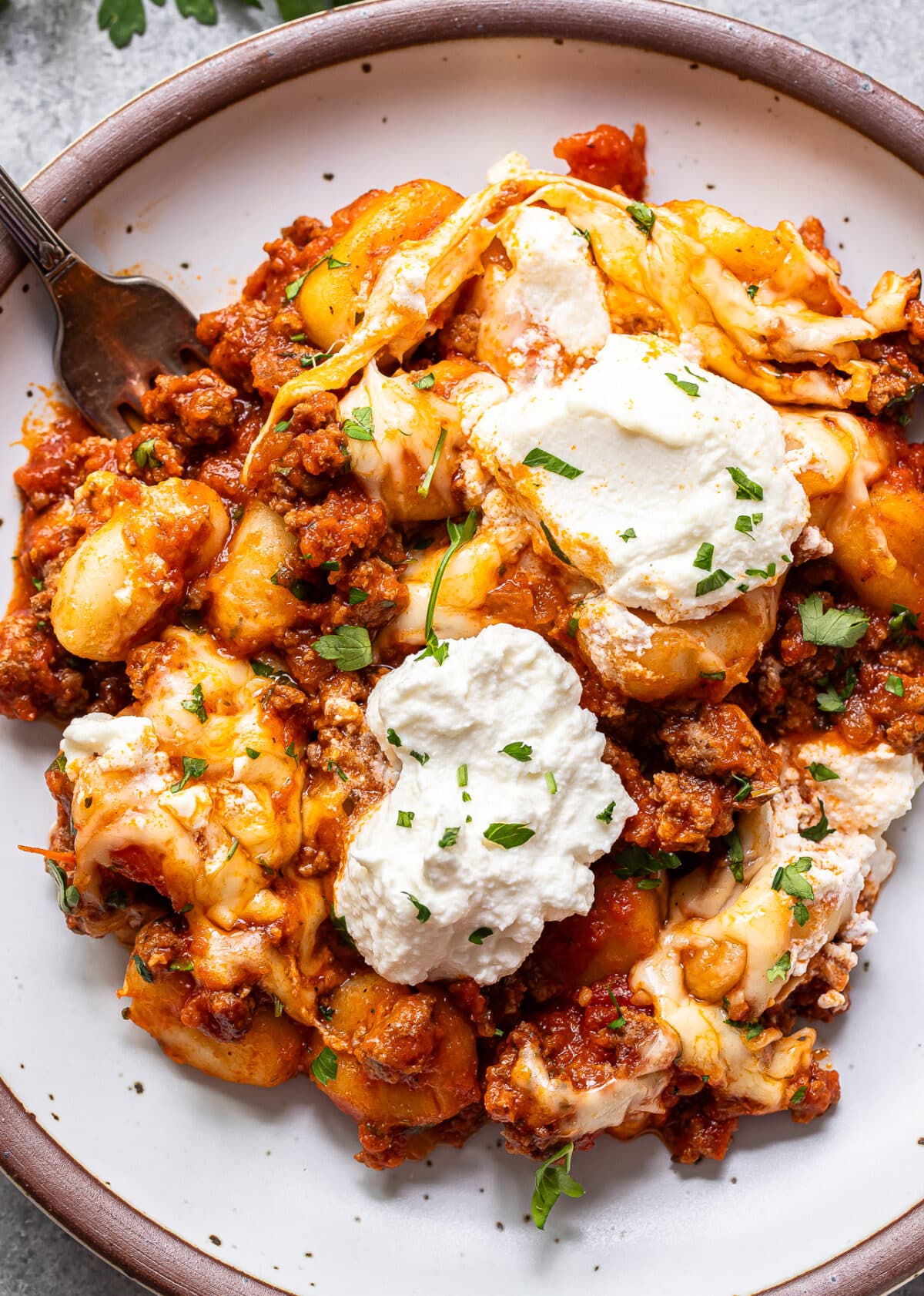 Ground beef gnocchi with marinara sauce, mozzarella, and ricotta on a white plate with a fork.