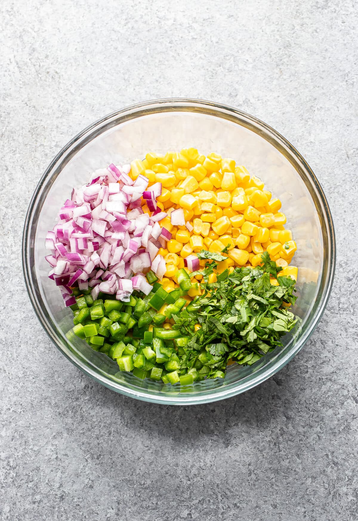 Corn, red onion, cilantro, jalapeno, and lime juice in a glass bowl.