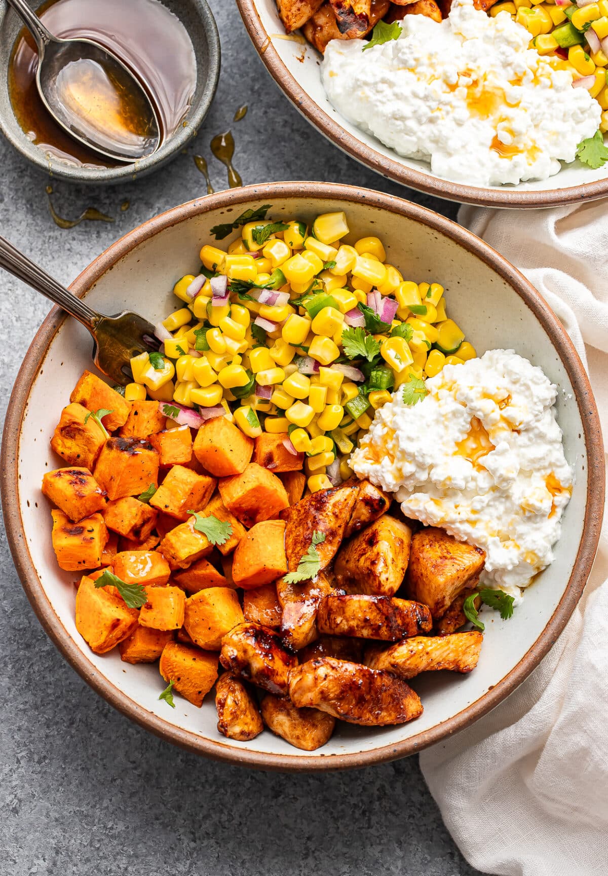 Hot honey chicken bowl with cottage cheese, sweet potatoes, and corn salsa in a white bowl with a fork. 