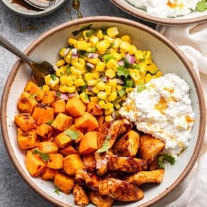 Hot honey chicken bowl with cottage cheese, sweet potatoes, and corn salsa in a white bowl with a fork.