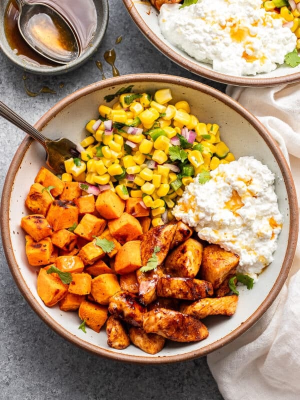 Hot honey chicken bowl with cottage cheese, sweet potatoes, and corn salsa in a white bowl with a fork.