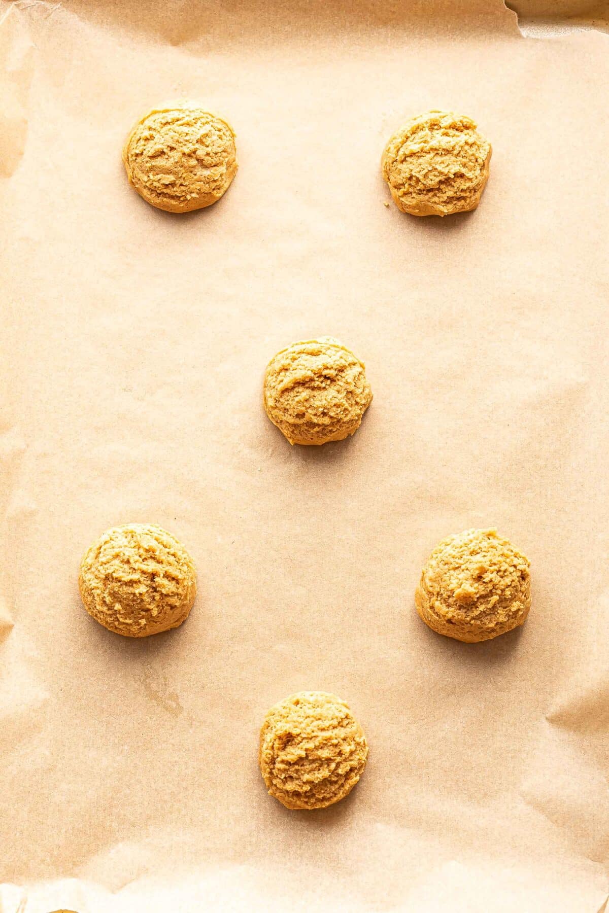 Six peanut butter cookie dough balls on a parchment paper lined baking sheet.