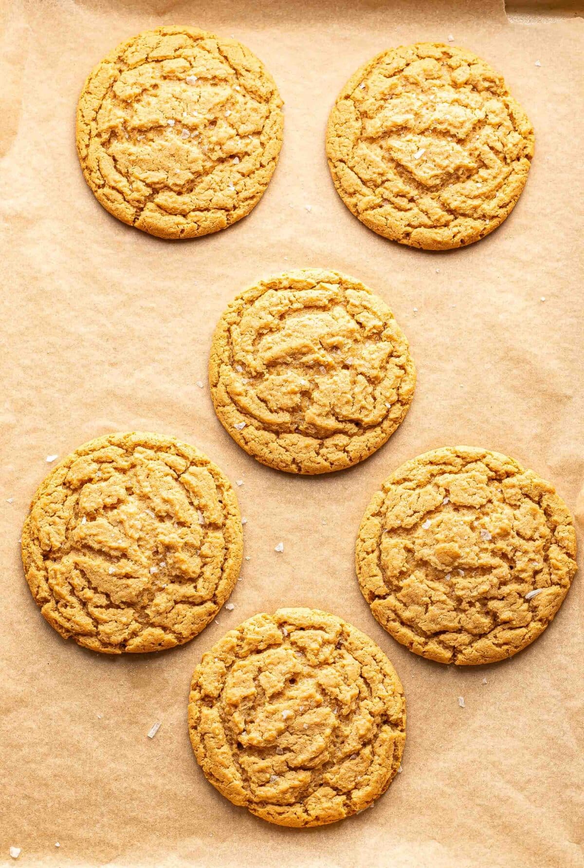 Six peanut butter cookies on a parchment paper lined baking sheet.