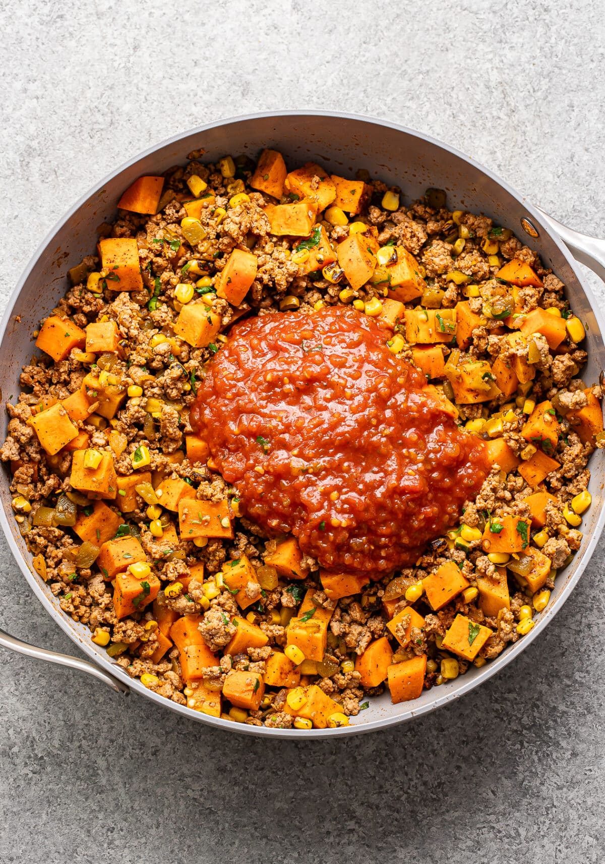 Ground turkey and sweet potatoes in a skillet with salsa on top before it's been stirred in.