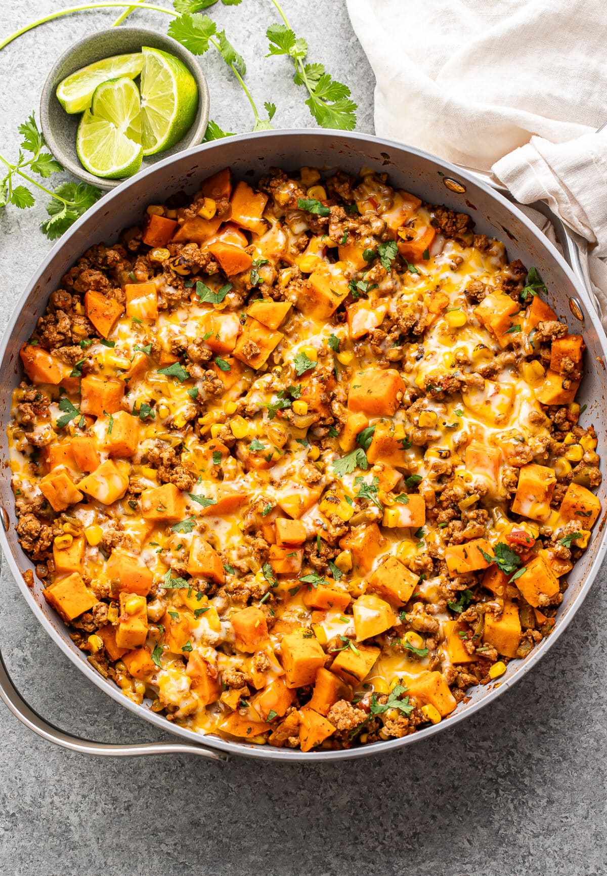 Southwest turkey sweet potato skillet with melted cheese on top and a dish with lime wedges behind it.