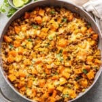 Southwest turkey sweet potato skillet with melted cheese on top and a dish with lime wedges behind it.