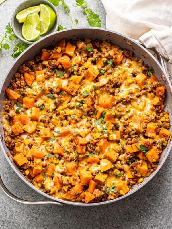 Southwest turkey sweet potato skillet with melted cheese on top and a dish with lime wedges behind it.