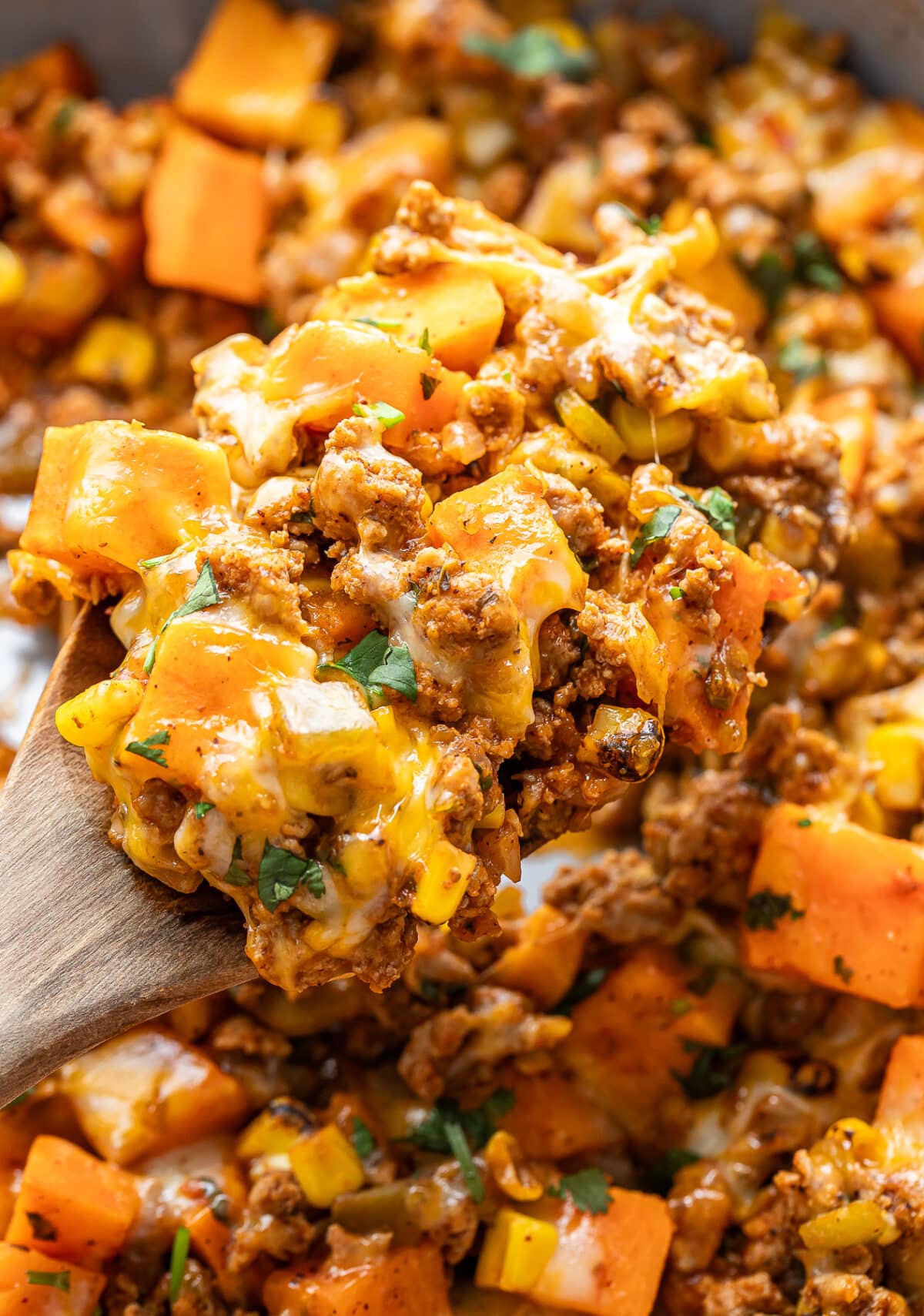 Wooden serving spoon scooping up ground turkey and sweet potatoes out of a skillet.