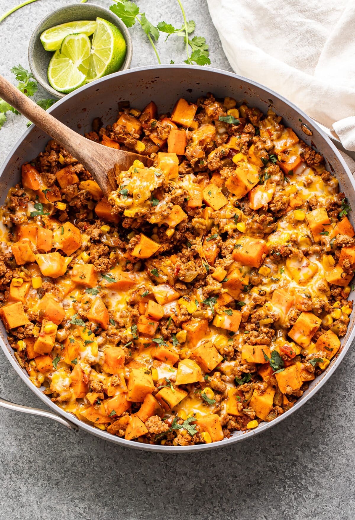 Southwest ground turkey and sweet potatoes topped with melted cheese in a skillet with a wooden serving spoon.