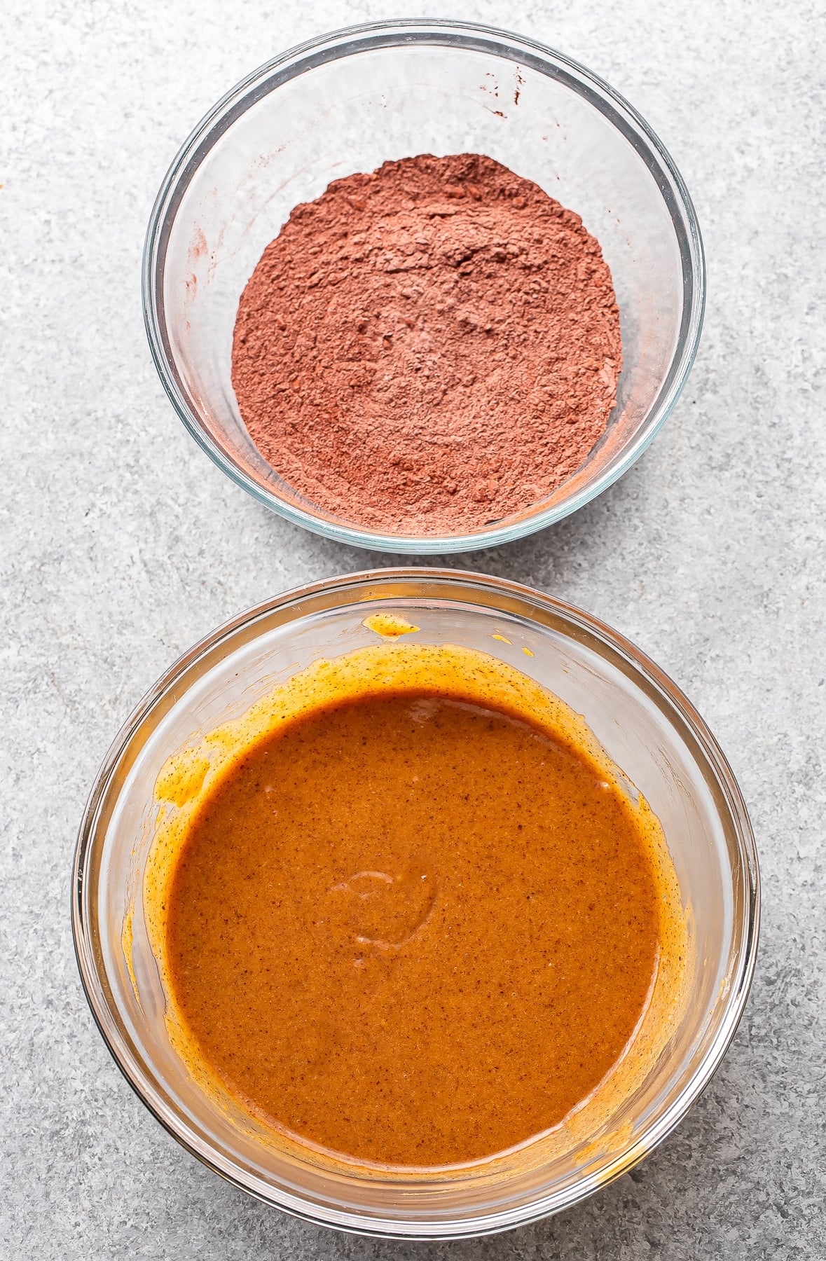 Wet ingredients for sweet potato brownies in a large glass bowl, dry ingredients in a smaller glass bowl.