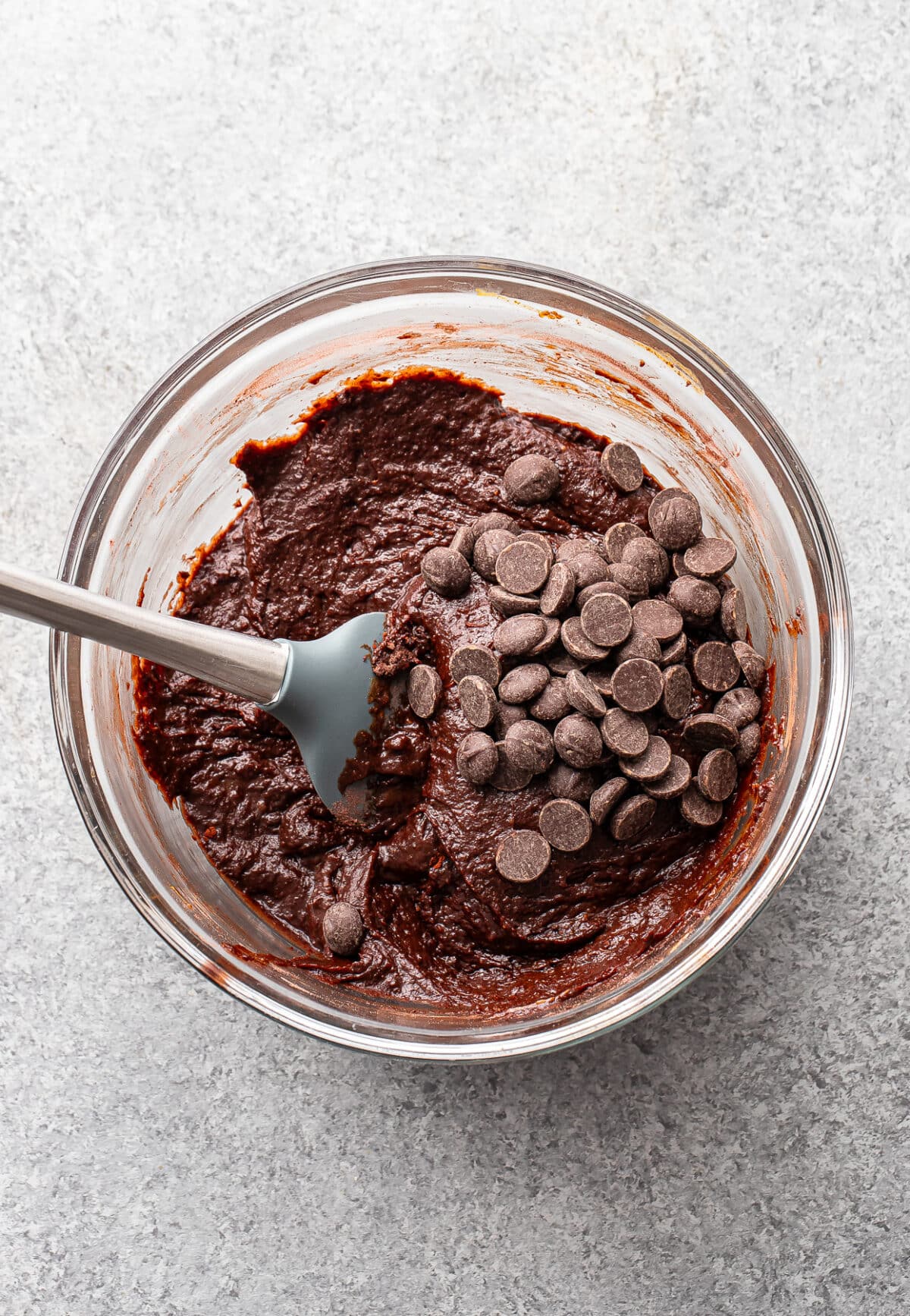 Sweet potato brownie batter with chocolate chips on top in a glass bowl with a rubber spatula.