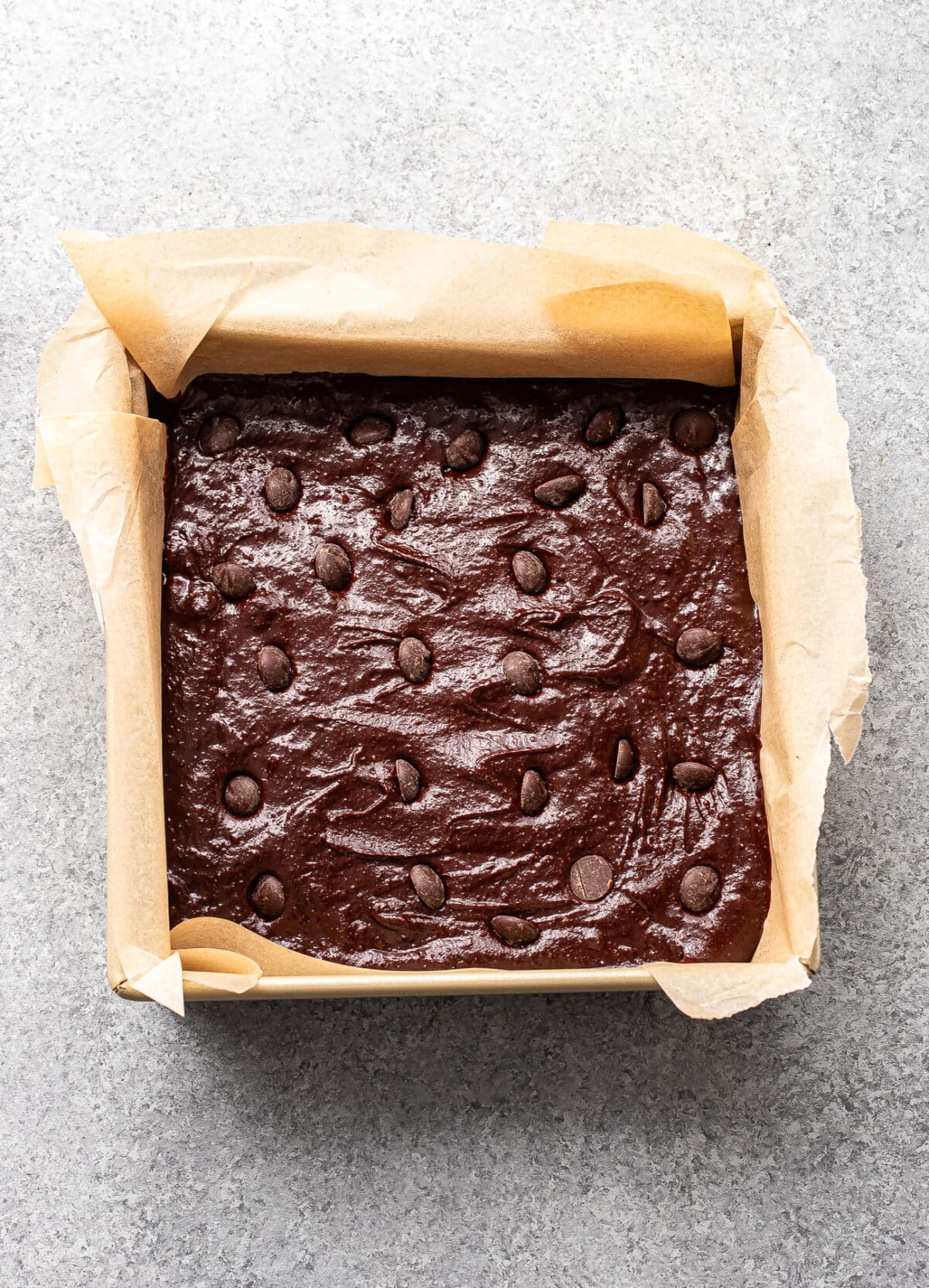 Sweet potato brownie batter in a parchment paper lined square baking pan.