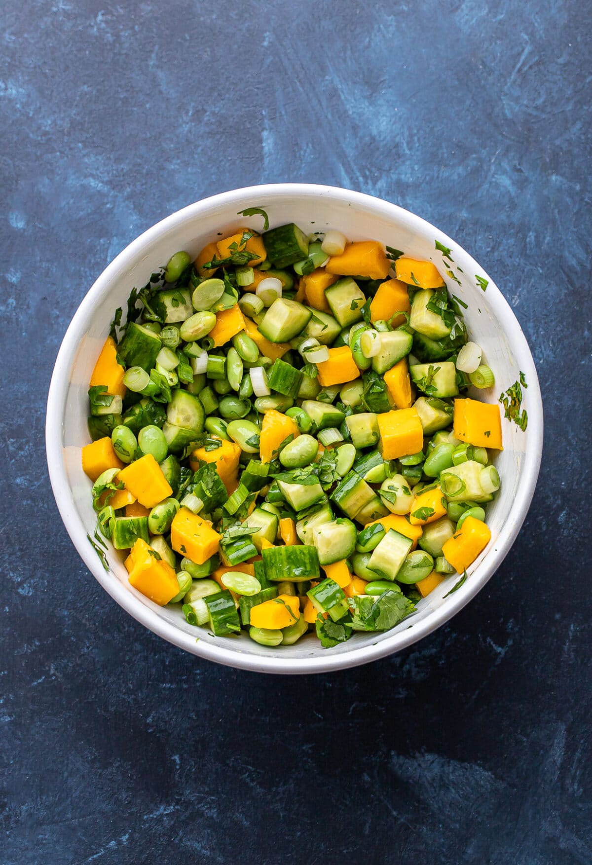 Mango, cucumber, edamame salad in a white mixing bowl.