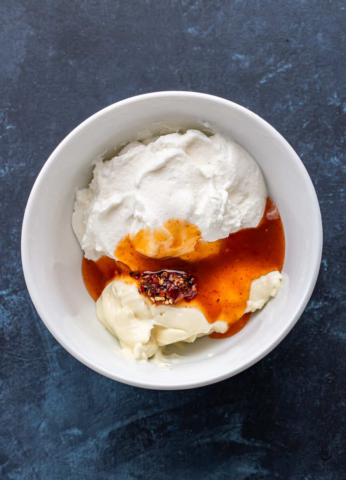 Mayo, Greek yogurt, chili crunch, and sweet chili sauce in a white bowl before being combined.