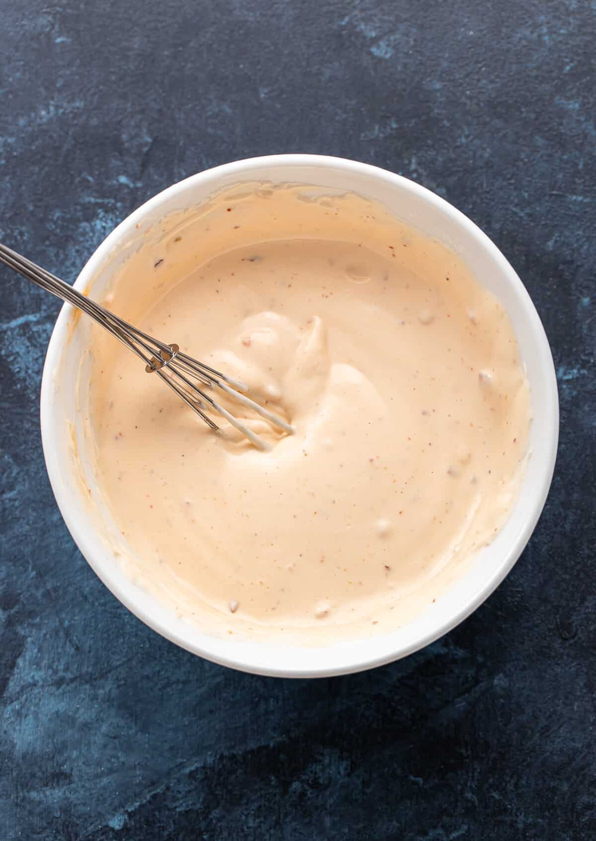 Sweet chili mayo in a white bowl with a whisk.