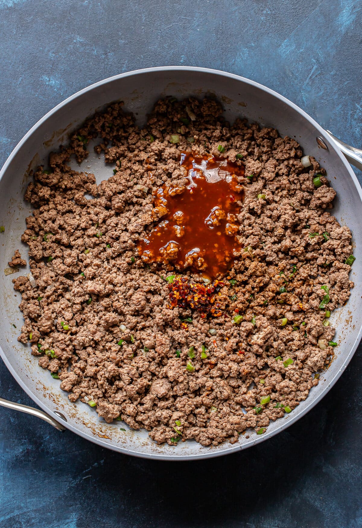 Cooked ground beef in a skillet with sweet chili sauce.