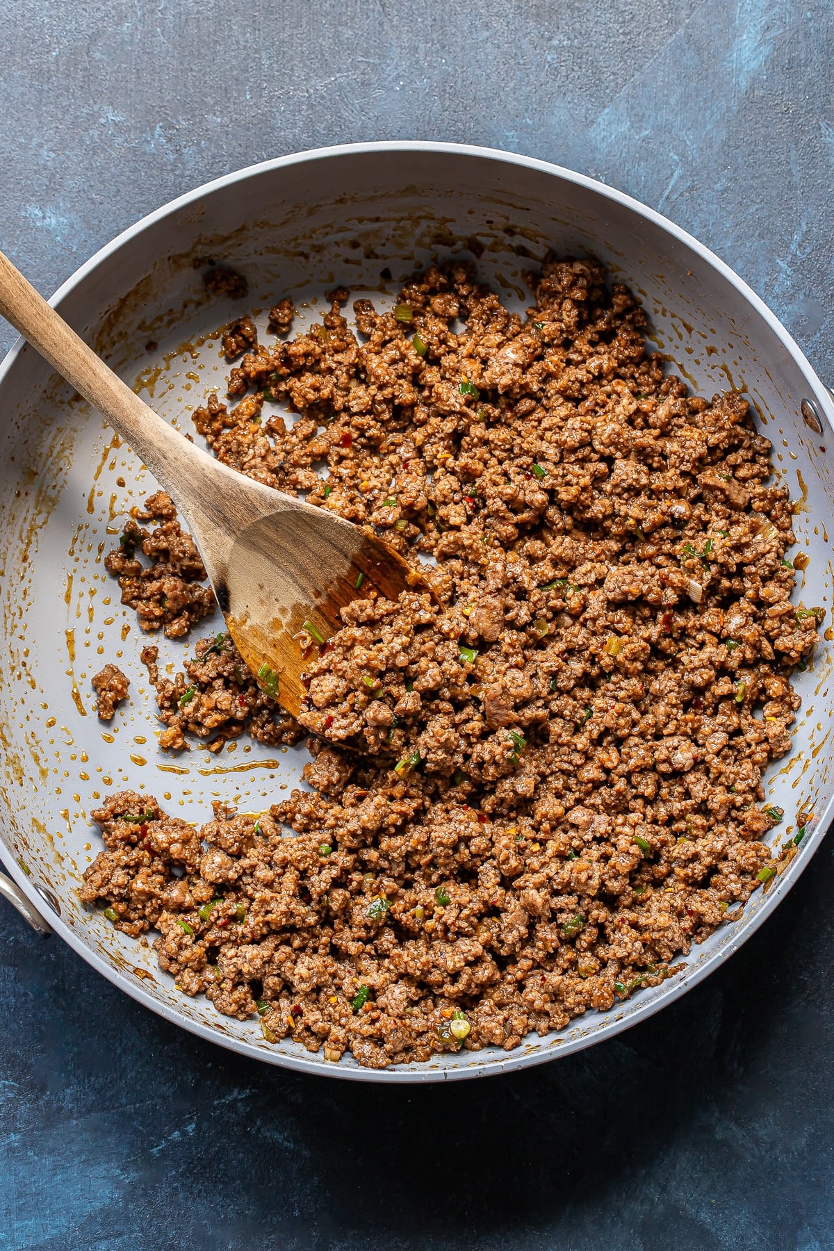 Sweet chili ground beef in a skillet with a wooden spoon.