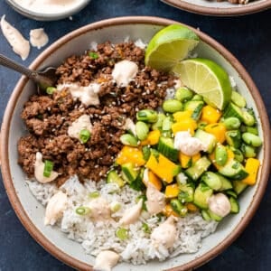 Asian beef bowl with cucumber mango salsa and rice in a white bowl with a fork.