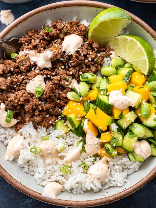 Asian beef bowl with cucumber mango salsa, rice and sweet chili mayo in a white bowl with a fork.