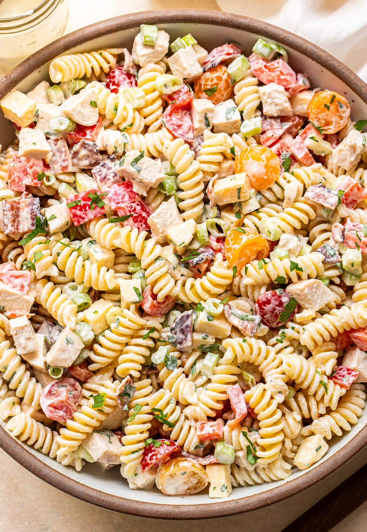 A close-up of a bowl filled with creamy rotini pasta salad, featuring diced chicken, cherry tomatoes, chopped green onions, and fresh herbs, all mixed in a creamy dressing.