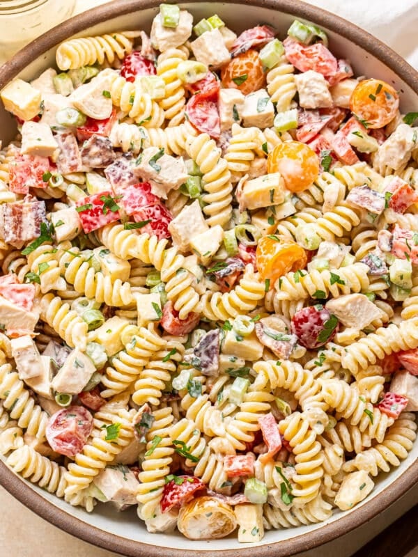 A close-up of a bowl filled with creamy rotini pasta salad, featuring diced chicken, cherry tomatoes, chopped green onions, and fresh herbs, all mixed in a creamy dressing.