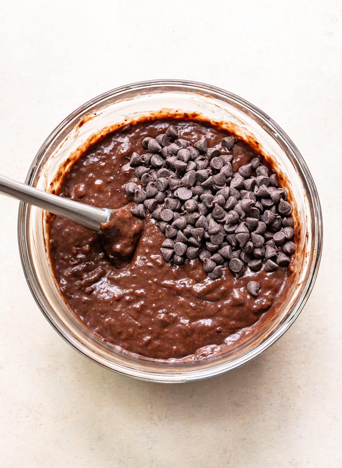 Chocolate banana bread batter with chocolate chips on top in a mixing bowl with a whisk.