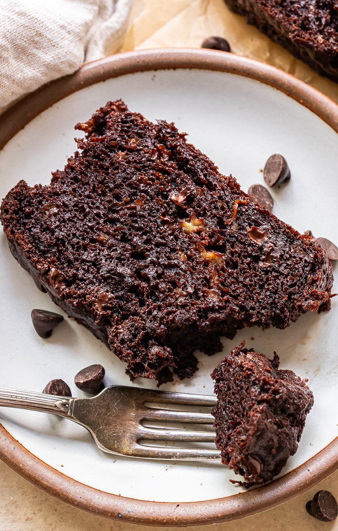 A white plate with a slice of chocolate banana bread with the corner cut off and on a fork.